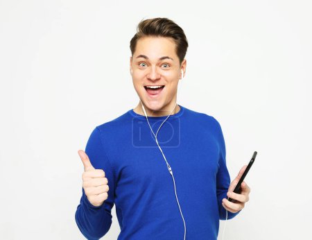 Téléchargez les photos : Lifestyle, happiness, emotional and people concept: Enjoying his favorite music. Happy young stylish man adjusting his headphones and smiling while standing against white background - en image libre de droit