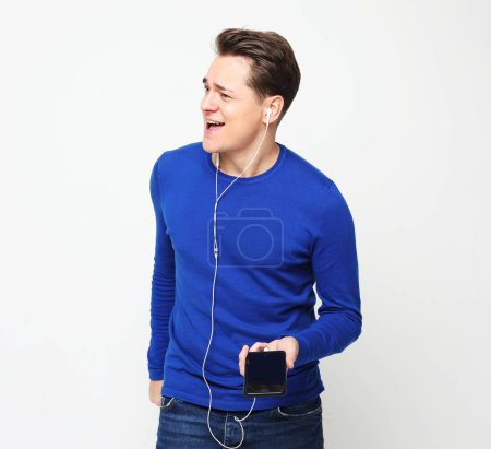 Téléchargez les photos : Lifestyle, happiness, emotional and people concept: Enjoying his favorite music. Happy young stylish man adjusting his headphones and smiling while standing against white background - en image libre de droit