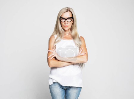 Téléchargez les photos : Elderly woman wearing eyeglasses standing over grey background. Old senior female, 60s gray-haired lady looking at camera arms crossed, portrait close up. - en image libre de droit