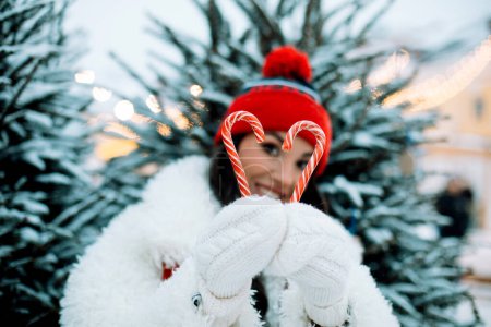 Foto de Joven alegre se ríe y lleva en sus manos piruletas de caramelo de Año Nuevo, feria de Navidad, invierno. Concepto de estilo de vida. - Imagen libre de derechos