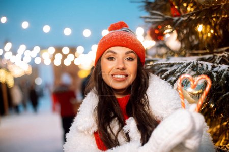 Photo for Cheerful young woman laughs and holds New Year's candy lollipops in her hands, Christmas fair, winter. Lifestyle concept. - Royalty Free Image