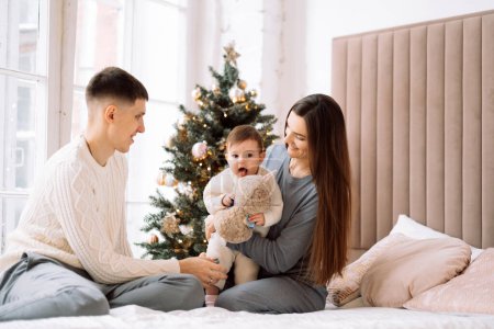 Photo for Happy young family - mom and dad together with little daughter next to christmas tree, have fun, enjoy happy family life. Lifestyle concept. - Royalty Free Image