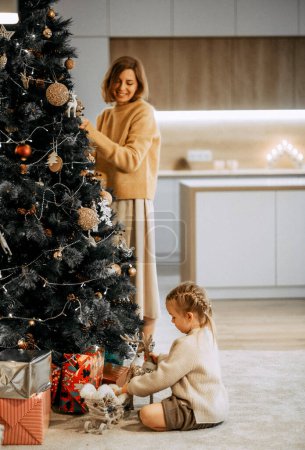 Téléchargez les photos : Merry Christmas and Happy Holidays. Mom and daughter decorate the Christmas tree indoors. The morning before Xmas. Lifestyle concept. - en image libre de droit