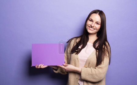 Photo for Fashion and beauty concept: Young woman holding purple blank advertising board standing on lilac background in studio - Royalty Free Image