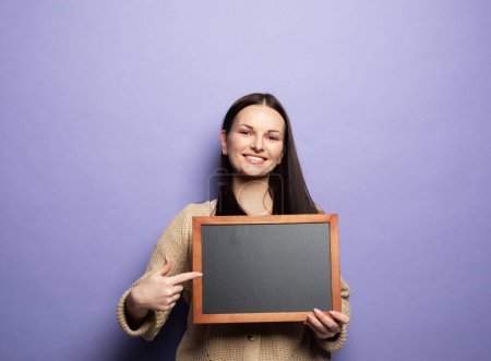 Téléchargez les photos : Young smiling student woman holding a chalkboard isolated on purple background. - en image libre de droit