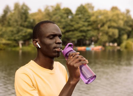 Photo for Young handsome and attractive black African American sport man tired and thirsty after running workout holding bottle drinking water or isotonic energy drink recovering in hydration concept - Royalty Free Image