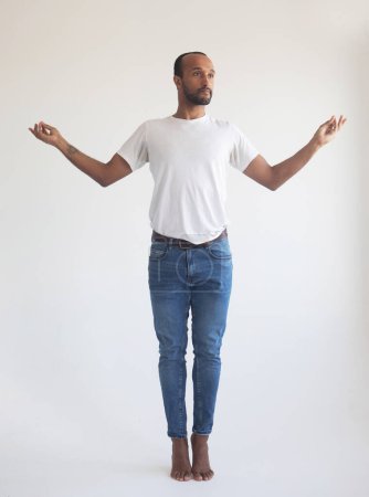 Téléchargez les photos : Jeune homme noir porte chemise blanche tenir écarter les mains dans yoga aum geste relax méditer essayer de se calmer isolé sur fond gris clair portrait studio - en image libre de droit