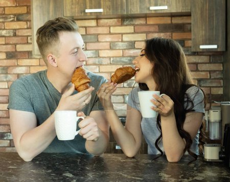 Foto de A young couple in love has breakfast in the kitchen, coffee and croissants, love and tenderness. - Imagen libre de derechos