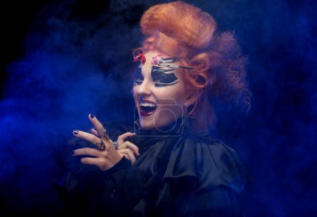 Téléchargez les photos : Halloween party. Young redhead woman dressed as a witch, posing over dark background. - en image libre de droit