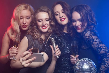 Foto de Group of partying women clinking flutes with sparkling wine and make selfie. Disco, party and people concept. - Imagen libre de derechos