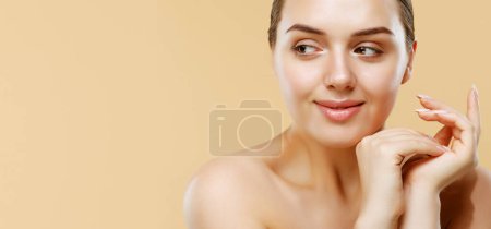 Téléchargez les photos : Happy beautiful woman holding her cheeks a laugh looking to the side.Young female with clean fresh skin. Beauty face care and treatment. Cosmetology and spa concept. Copy space. - en image libre de droit