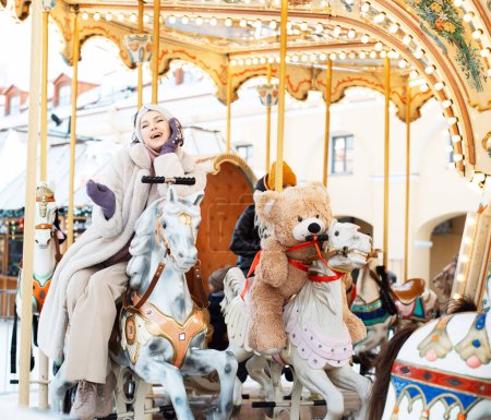 Téléchargez les photos : Pretty woman saddled a horse on a carousel. Christmas market, happiness and fun. - en image libre de droit