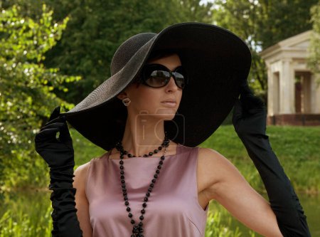 Foto de Hermosa joven hembra en un gran sombrero negro camina en el parque, estilo vintage. Mujer retro. Hora de verano. - Imagen libre de derechos
