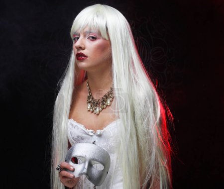 Foto de Concepto de fiesta y moda: Hermosa mujer joven con el pelo largo y blanco sosteniendo una máscara de carnaval de plata - Imagen libre de derechos