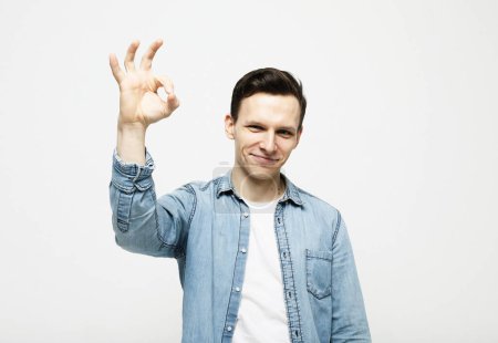 Photo for Lifestyle and people concept: Portrait of a cheerful young man showing okay gesture isolated on the white background - Royalty Free Image