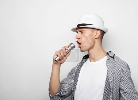 Téléchargez les photos : Young handsome man wearing white hat singing with microphone over grey background - en image libre de droit