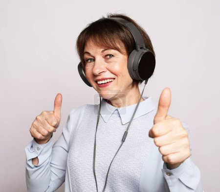 Foto de Estilo de vida, tehnología y concepto de la gente: Mujer mayor escuchando música y mostrando los pulgares hacia arriba sobre el fondo blanco - Imagen libre de derechos