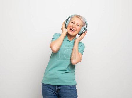 Photo for People, tehnology, aging and maturity concept. Happy elderly short haired woman in wireless headphones. Dance over grey background. - Royalty Free Image