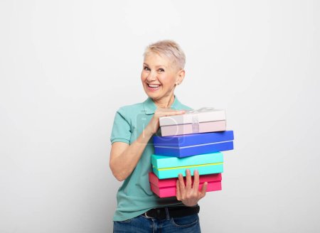 Photo for Party, birthday and old people concept: Elderly smiling happy caucasian cheerful cool woman 60s with short hair, wearing casual, holding present boxex with gifts isolated on white grey background - Royalty Free Image