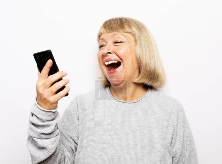 Photo for Lifestyle, tehnology and modern old people concept: Portrait of attractive blond senior woman talking by mobile phone over white background - Royalty Free Image