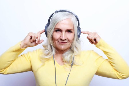Téléchargez les photos : Femme âgée joyeuse écoutant de la musique avec des écouteurs sur fond blanc. Style de vie et concept de personnes. - en image libre de droit
