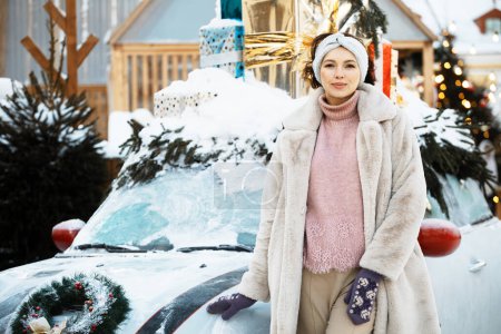 Téléchargez les photos : Belle jeune femme en vêtements d'hiver à côté d'une voiture décorée avec le décor du Nouvel An au marché de Noël - en image libre de droit