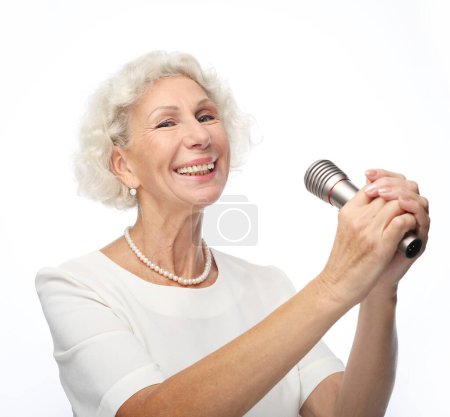 Foto de Emoción, estilo de vida y concepto de ancianos: Mujer mayor feliz con el pelo rizado cantando con micrófono, divirtiéndose, expresando talento musical - Imagen libre de derechos