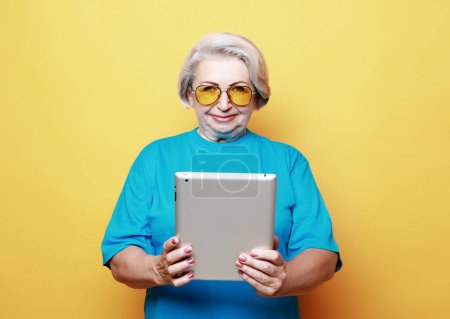 Téléchargez les photos : Photo of old attractive lady use tablet isolated over yellow background - en image libre de droit