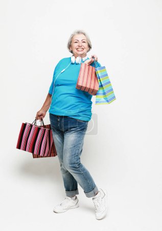 Photo for Full length photo of positive cheerful grey white hair elderly woman enjoy leisure time shopping hold bags wear jeans and blue shirt isolated over white background - Royalty Free Image