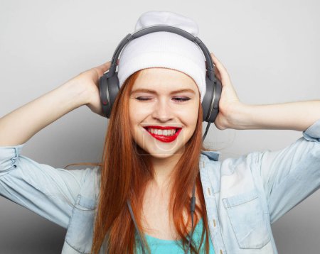 Foto de Estilo de vida, la moda y el concepto de la gente: mujer pelirroja joven con auriculares escuchando música. Estilo Hipster. - Imagen libre de derechos