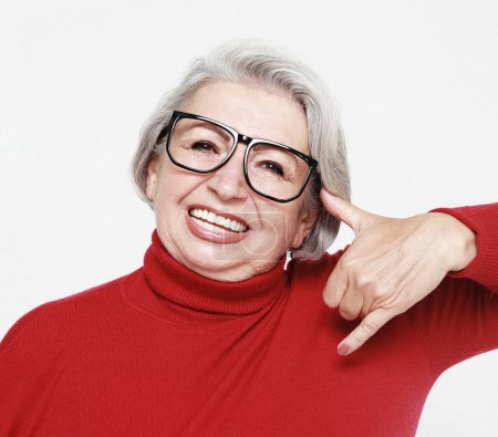 Photo for Senior happy woman wearing red sweater and glasses is making a call me gesture, isolated on white background - Royalty Free Image