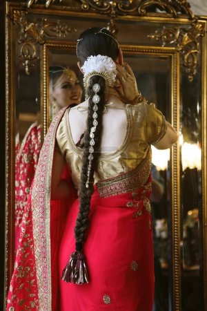 Foto de Female model Hindu Bride in saree, wearing gold and jasmine flower garlands in the hair near mirror, back view. - Imagen libre de derechos