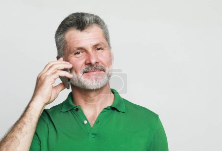 Téléchargez les photos : Lifestyle, tehnology and old people concept: smiling senior bearded man speaking on the phone with somebody over grey background - en image libre de droit