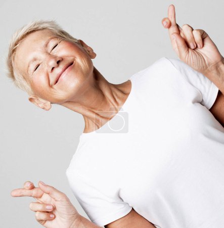Foto de Senior caucasian woman with short hair thinking about something pleasant and making wish with crossed fingers isolated over grey background - Imagen libre de derechos