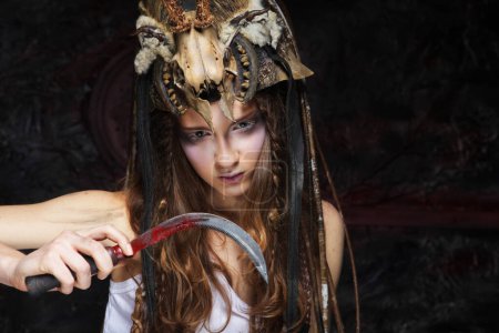 Foto de Mujer joven con maquillaje agresivo sosteniendo una hoz. Halloween. Fiesta de disfraces. - Imagen libre de derechos
