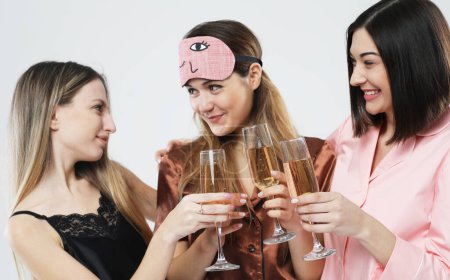 Foto de Three young happy women dressed in pajamas drink champagne and have fun, pajama party and friendship concept. - Imagen libre de derechos