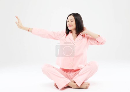 Téléchargez les photos : Jeune jolie femme asiatique en pyjama rose assise sur le sol et étirant, étirant, yoga, éveil. - en image libre de droit