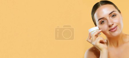 Foto de Skincare- Mujer bonita joven sosteniendo crema cosmética sobre fondo beige - Imagen libre de derechos