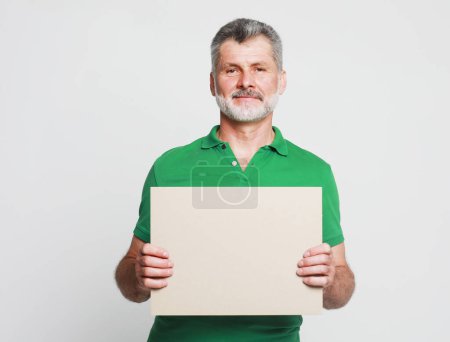 Photo for Happy mature bearded man in green shirt with blank advertising board over grey background, free space - Royalty Free Image