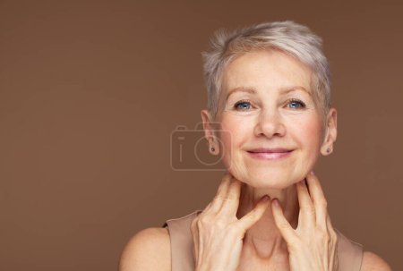 Téléchargez les photos : Portrait de beauté de femme mûre souriant avec la main sur le visage. Visage rapproché d'une femme âgée heureuse se sentant fraîche après un traitement anti-âge. Beauté souriante regardant la caméra avec une peau parfaite. - en image libre de droit