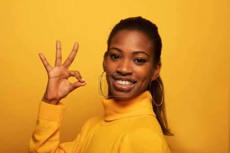 Photo for Beautiful young african american woman signaling ok, isolated over yellow background - Royalty Free Image