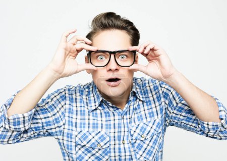 Foto de Young man wearing blue casual plaid shirt clothes and glasses surprised and shocked with excited face over white background - Imagen libre de derechos