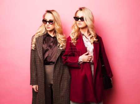 Foto de Fashion and beauty concept: Two sweet young women posing in nice clothes, coat, handbag. Sisters, twins. Spring fashion photo. - Imagen libre de derechos