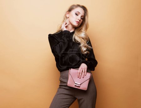 Foto de Beautiful young blond woman in a blouse and pants holding handbag posing over beige background. - Imagen libre de derechos