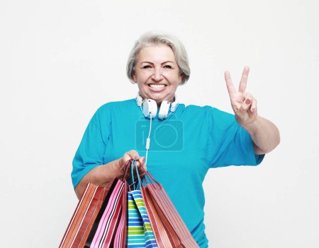 Photo for Lifestyle, shopping and old people concept: Happy elderly woman with shopping bags show victory sign isolated on white background - Royalty Free Image