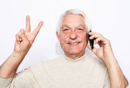Téléchargez les photos : Portrait of positive old man hold new cellphone show v-sign sign recommend choose good modern technology. Mature male Posing over white background. - en image libre de droit