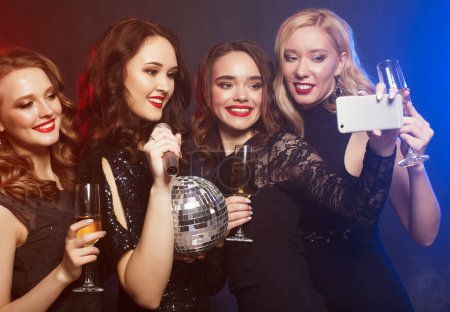 Téléchargez les photos : Group of partying women clinking flutes with sparkling wine and make selfie. Disco, party and people concept. - en image libre de droit