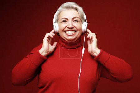 Téléchargez les photos : Lifestyle, party, emotion and old people concept: elderly woman wearing red sweater listening to music with headphones - en image libre de droit