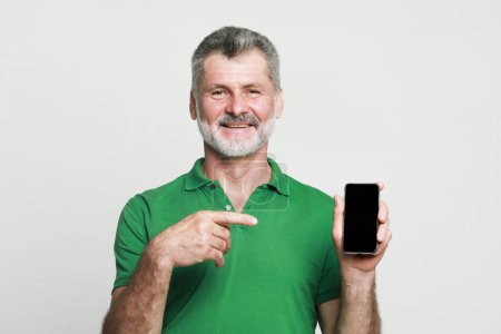 Téléchargez les photos : Lifestyle, tehnology and people concept: A picture of mature bearded man with new smartphone, points a finger at the screen, advertises the phone. - en image libre de droit