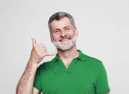 Téléchargez les photos : Photo of aged bearded man happy positive smile show finger call phone sign over grey background. - en image libre de droit